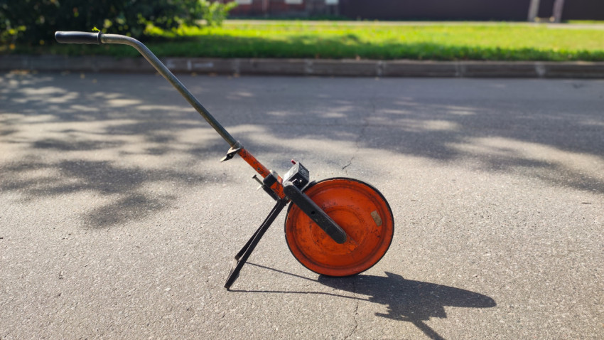 Мерное колесо со стойкой и длинной тенью на зернистом асфальте