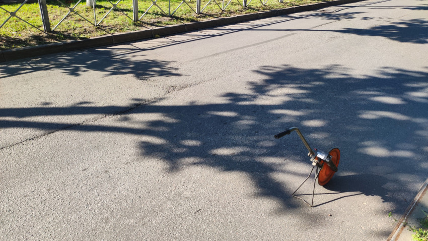 Измерительное колесо стоит на асфальте у бордюра в солнечную погоду