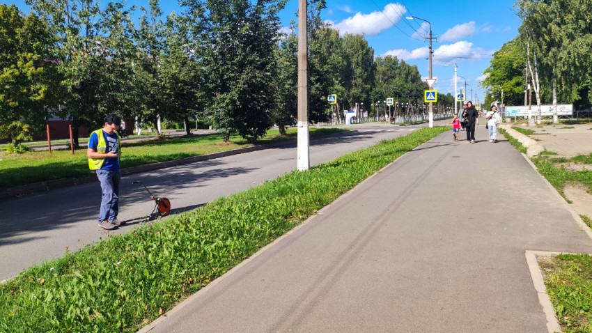 Рабочий с мерным колесом на дороге, прохожие и дорожные знаки на заднем плане