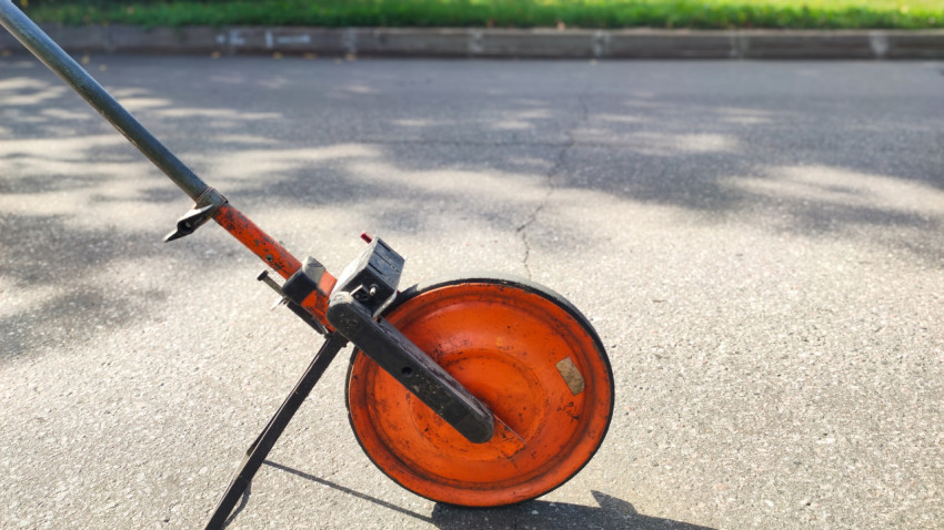 Оранжевое измерительное колесо крупным планом на солнечном асфальте