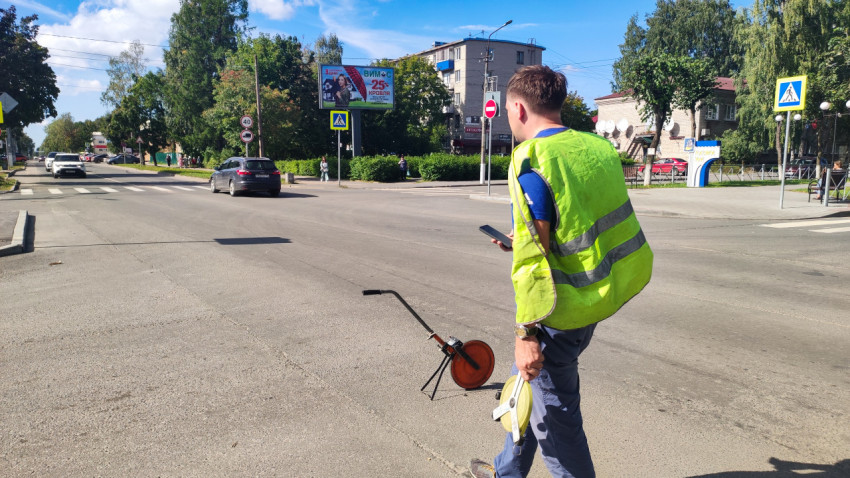 Рабочий с измерительным колесом делает замер на дороге у перехода