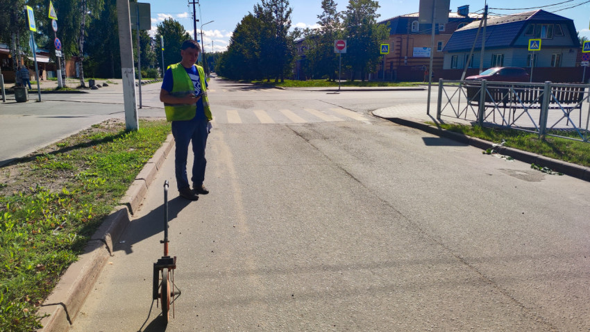 Измерительное колесо у бордюра и рабочий в сигнальном жилете рядом с пешеходным переходом