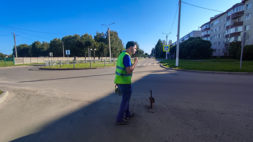 Рабочий в сигнальном жилете отмечает точку замера рядом с измерительным колесом на перекрёстке