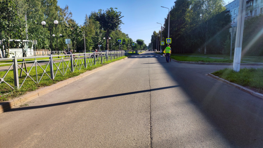 Прямая улица с ограждением и знаками перехода, вдали идёт рабочий с измерительным колесом