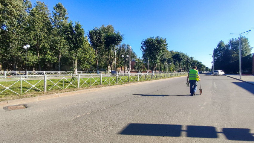 Человек с измерительным колесом катит его вдоль пустой улицы и снимает замеры