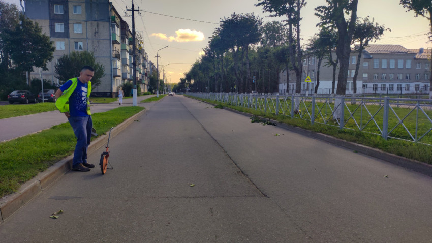 Парень в сигнальном жилете катит мерное колесо по дороге перед проверкой ровности покрытия
