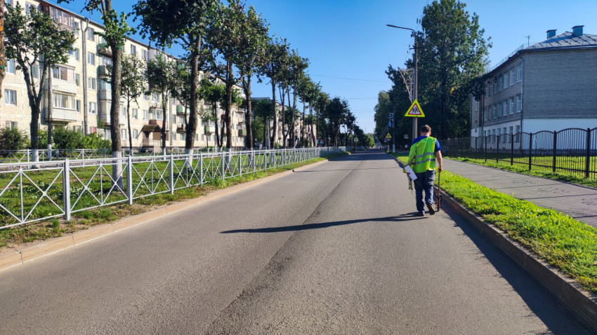 Парень в сигнальном жилете меряет участок дороги мерным колесом