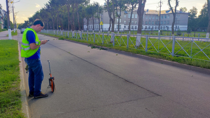 Дорожник с измерительным колесом стоит на пустой улице и фиксирует замеры на телефон