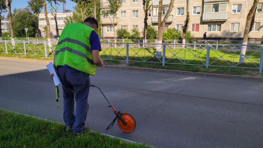 Мужчина в сигнальном жилете держит документы рядом с мерным колесом на городской улице