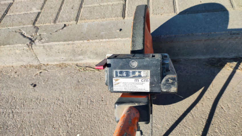 Счётчик измерительного колеса показывает метры и сантиметры на фоне бордюра и тротуара