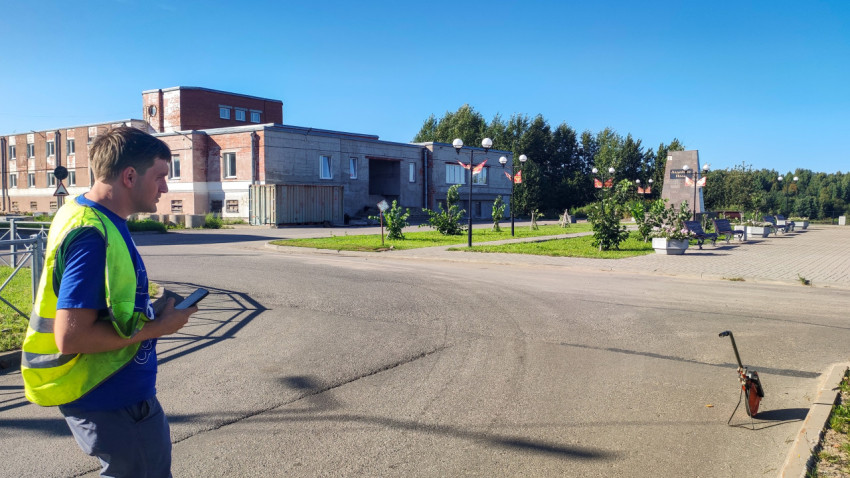 Рабочий проверяет замеры в телефоне, пока курвиметр стоит у края дороги на площади