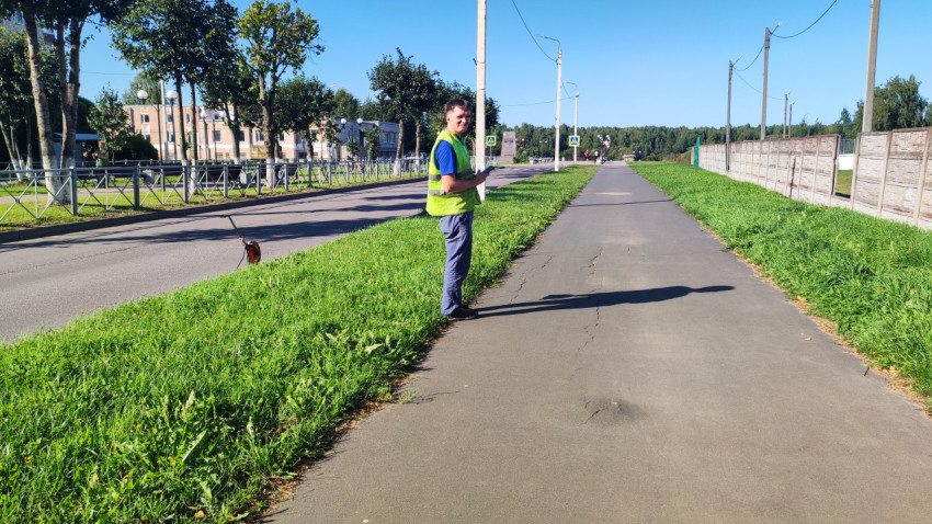 Рабочий сверяет данные в телефоне, а курвиметр стоит на траве у бордюра