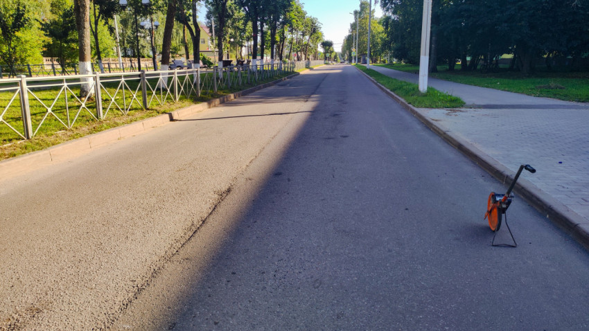 Измерительное колесо стоит на дороге, а улица уходит вдаль между деревьями