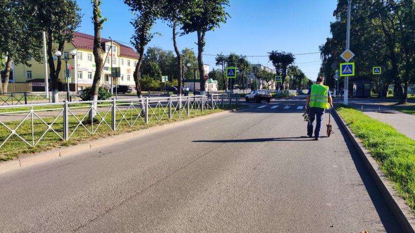 Дорожный рабочий в жилете катит измерительное колесо по пустой улице у пешеходного перехода