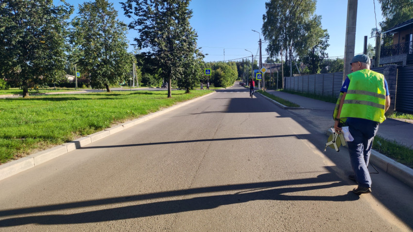 Рабочий с измерительным колесом идёт по дороге к пешеходному переходу, навстречу едет велосипедист