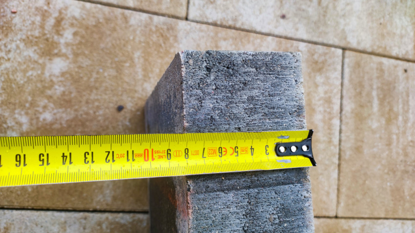 Замер ширины бетонного бордюрного камня рулеткой крупным планом