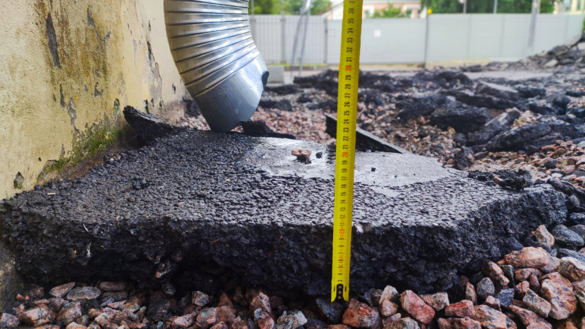 Водосточная труба и измерительная рейка на участке демонтажа покрытия