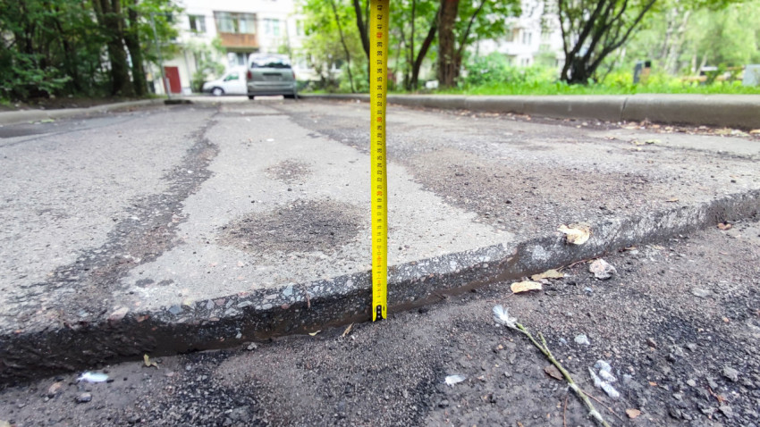 Замер перепада асфальтового покрытия рулеткой на дворовой дороге с разрушенной кромкой