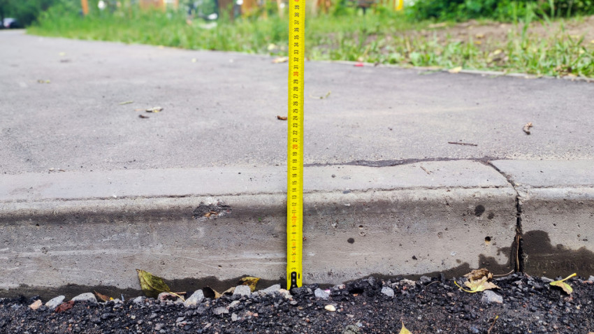 Измерение высоты бордюрного камня рулеткой на границе асфальта и щебня