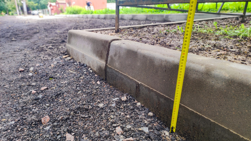 Измерение рулеткой высоты бордюра у щебёночного основания в дворовой зоне