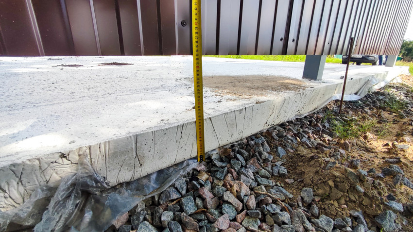Измерение высоты бетонной плиты рулеткой у кромки ограждения из профлиста и щебёночной отсыпки