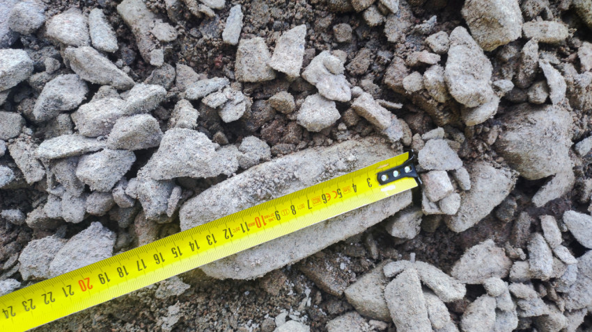 Жёлтая рулетка на обломках бетона и каменной крошке при проверке фракции материала