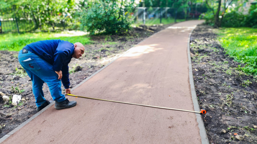 Рабочий измеряет ширину новой дорожки рулеткой на участке благоустройства