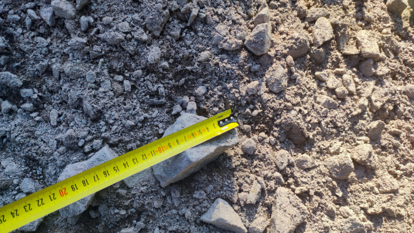 Измерение фрагмента бетонного лома рулеткой на россыпи щебня и строительного мусора