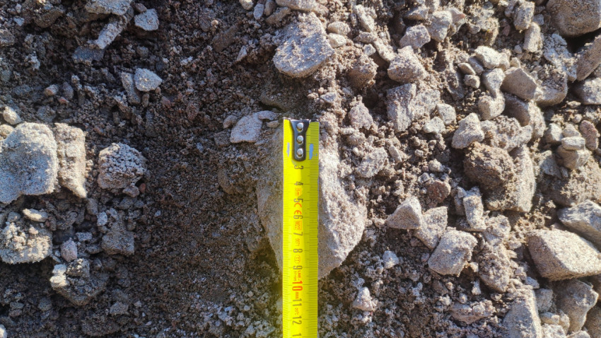 Рулетка измеряет размер куска бетона в смеси щебня и песка на ремонтируемом основании