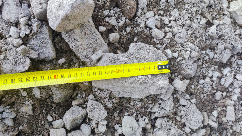 Рулетка с металлическим зацепом на россыпи бетонных обломков и щебня, вид сверху