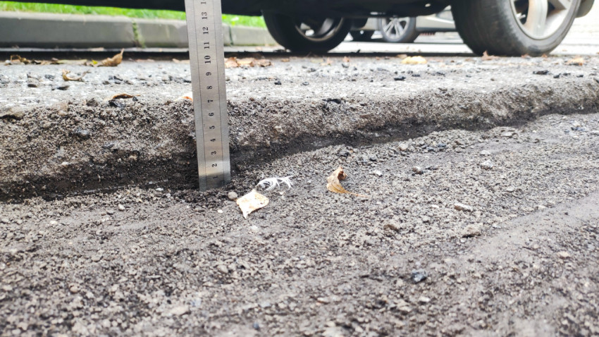 Линейка измеряет глубину колеи и выборки в асфальтовой крошке у бордюра рядом с колесом автомобиля