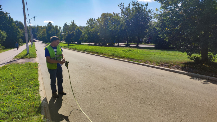 Рабочий в жилете растянул рулетку поперёк проезжей части для замера ширины