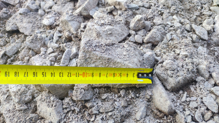 Замер крупного фрагмента в насыпи щебня рулеткой для строительного контроля на объекте