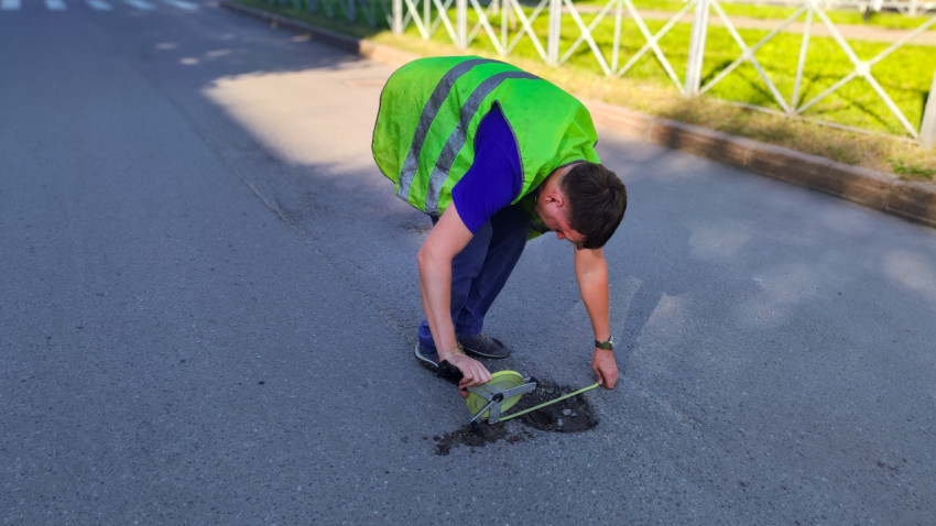 Дорожник меряет выбоину рулеткой прямо на проезжей части