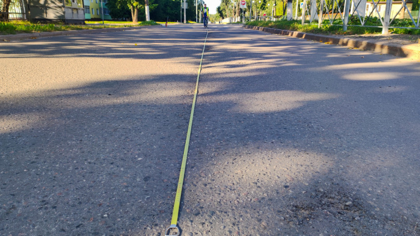 Рулетка с кольцом на конце лежит на асфальте и уходит к дорожнику в перспективу улицы