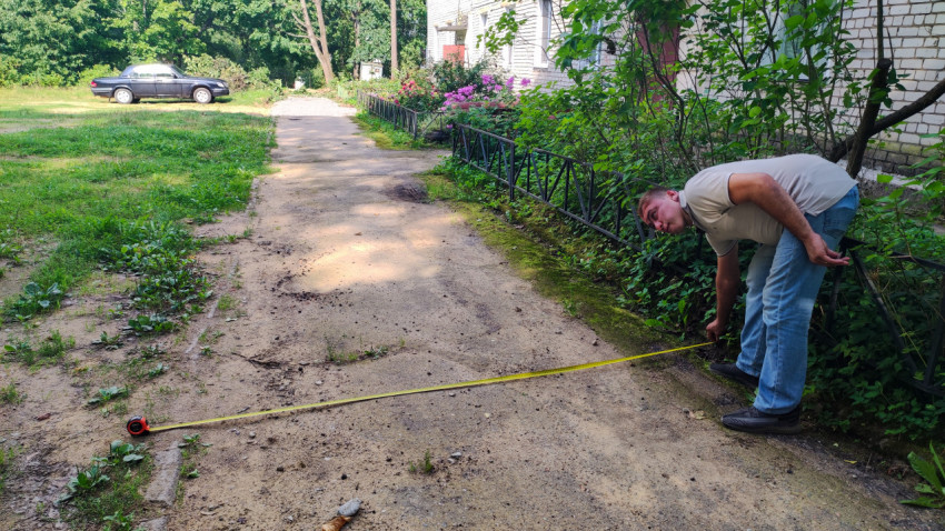 Измерение ширины пешеходной дорожки рулеткой во дворе жилого дома