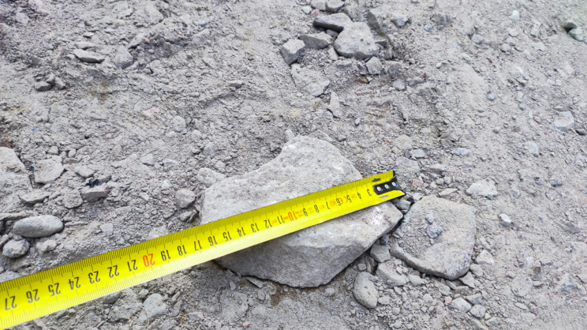 Замер размера крупного камня строительной рулеткой на щебёночной подсыпке при подготовке основания