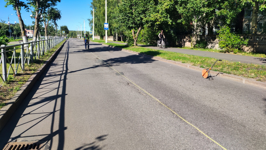 Рулетка через трещину на дороге, рабочий делает замер, рядом велосипедист и измерительное колесо