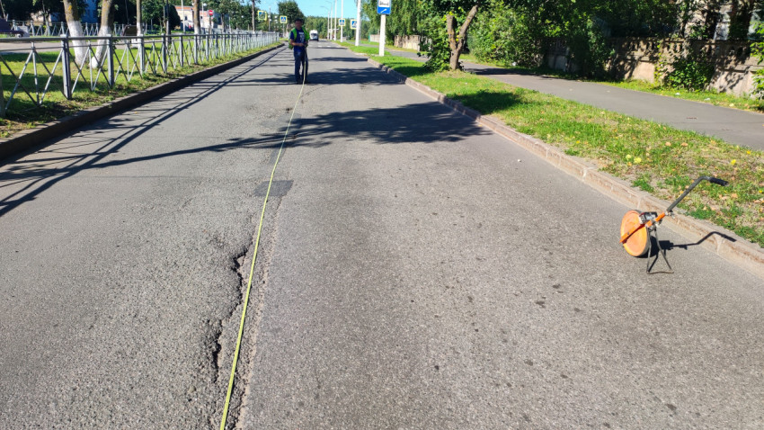 Лентой и мерным колесом измеряют длину трещины на асфальтовой дороге