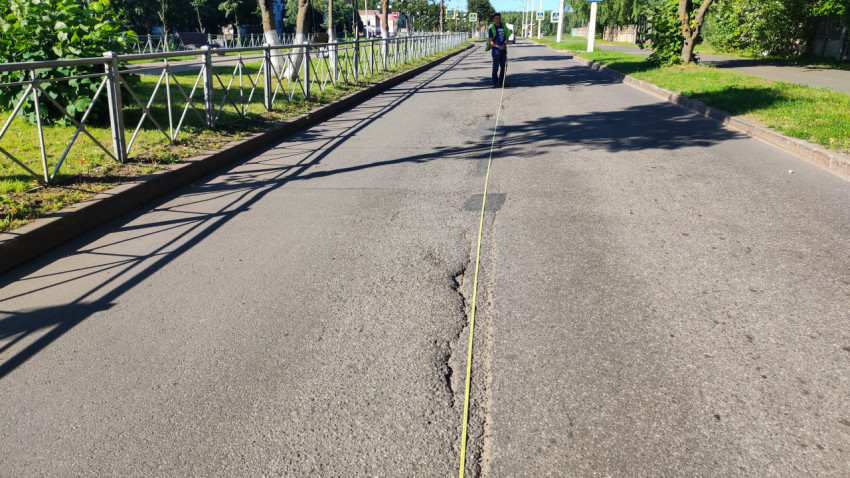 Замер рулеткой вдоль дефекта асфальта рядом с ограждением и зелёной обочиной
