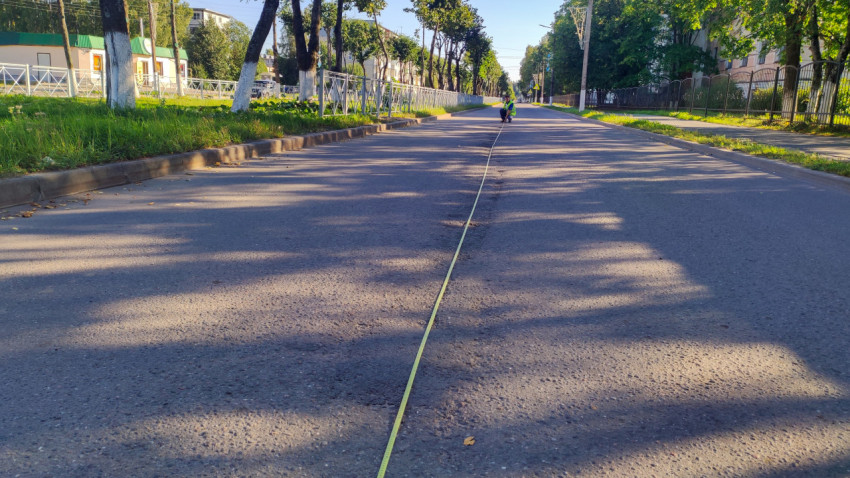 Длинная рулетка растянута по дороге, а инспектор в жилете фиксирует замер на расстоянии