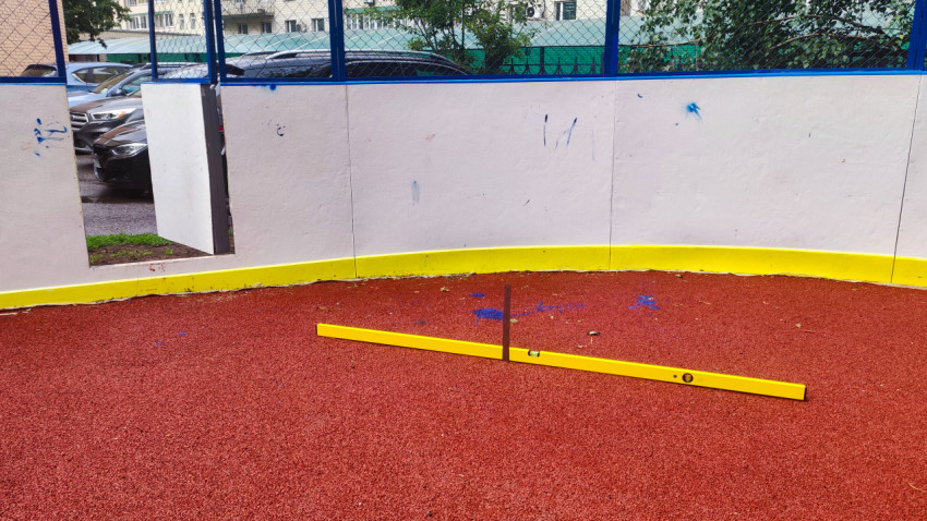 Проверка ровности резинового покрытия уровнем на огороженной спортплощадке