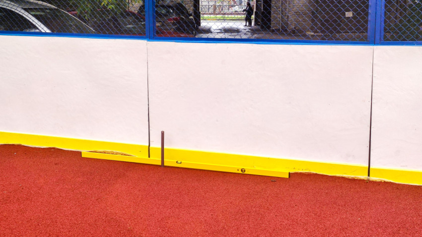 Замер у основания борта спортплощадки: уровень, линейка и деформированный жёлтый отбойник