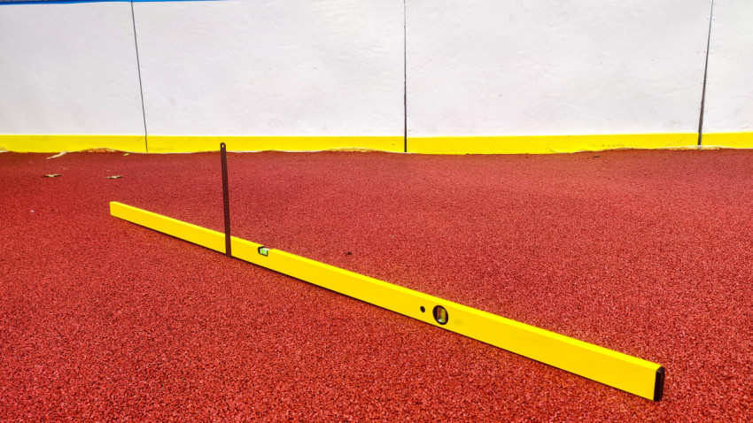 Строительный уровень на резиновом покрытии у борта спортивной площадки