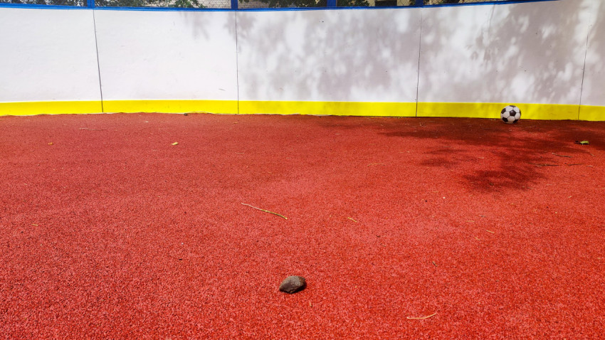 Камень на покрытии дворовой площадки рядом с футбольным мячом