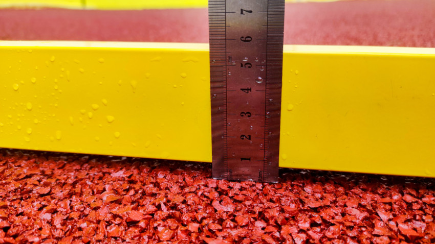 Контроль ровности резинового покрытия строительным уровнем у борта спортплощадки