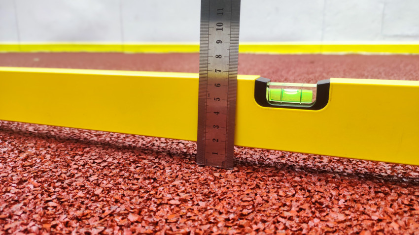 Крупный план замера зазора линейкой рядом с пузырьковым уровнем на резиновой крошке