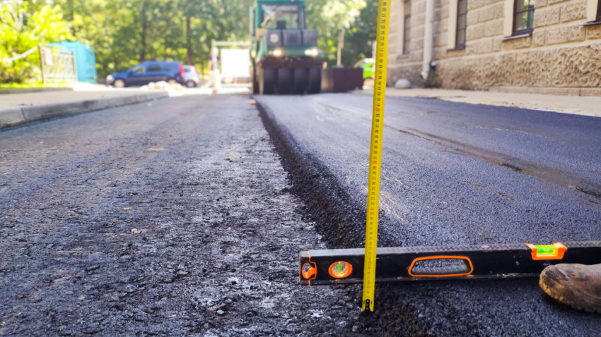 Рулетка и строительный уровень на шве асфальта при проверке примыкания покрытия