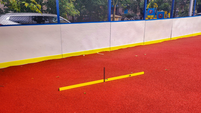 Проверка ровности резинового покрытия в спортивной коробке уровнем