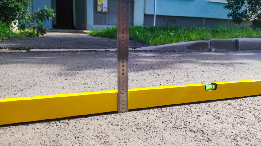 Крупный план пузырькового уровня и металлической рейки при замере перепада на дороге